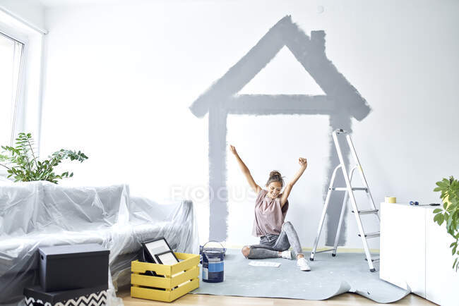 Lächelnde Frau mit erhobener Hand sitzt zu Hause gegen Wand — Stockfoto