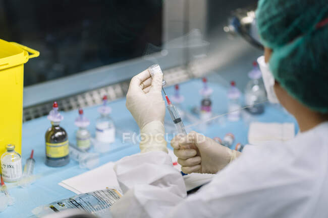 Primer plano de la farmacia femenina inyectando líquido en el vial en el laboratorio - foto de stock