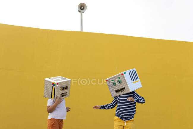 Friends wearing robot costumes standing against yellow wall - foto de stock