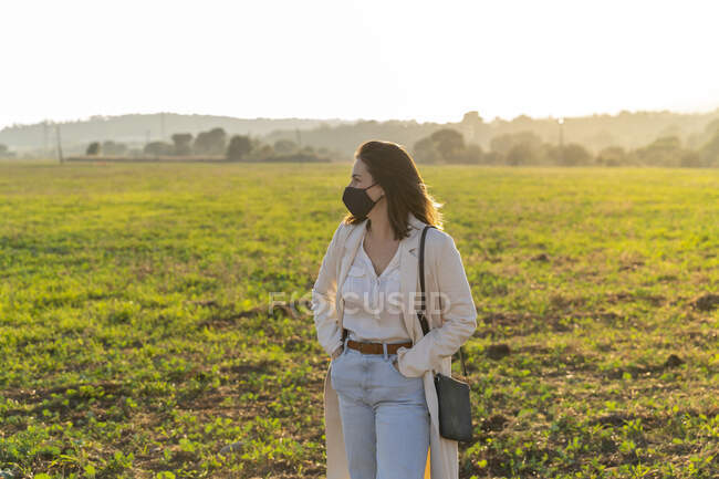 Young woman wearing protective face mask while enjoying countryside during pandemic — Stock Photo