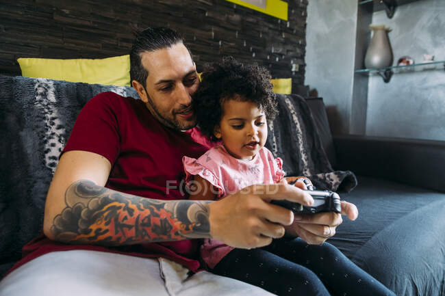 Батько з донькою грається в відеоігри, а вдома відпочиває на дивані. — стокове фото