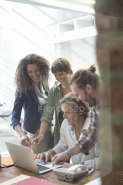 Усміхнена команда працівників, які працюють на ноутбуці, стоячи при владі. — стокове фото