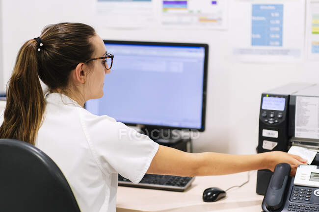 Farmacista femminile con fax alla scrivania mentre è seduta in ospedale — Foto stock