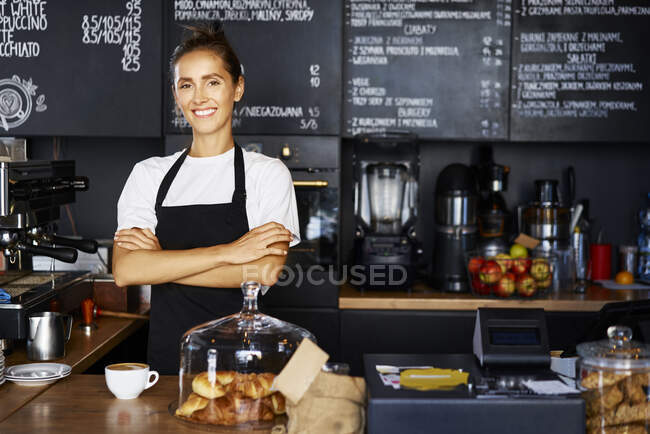 Портрет улыбающейся официантки со скрещенными руками, работающей в кафе — стоковое фото