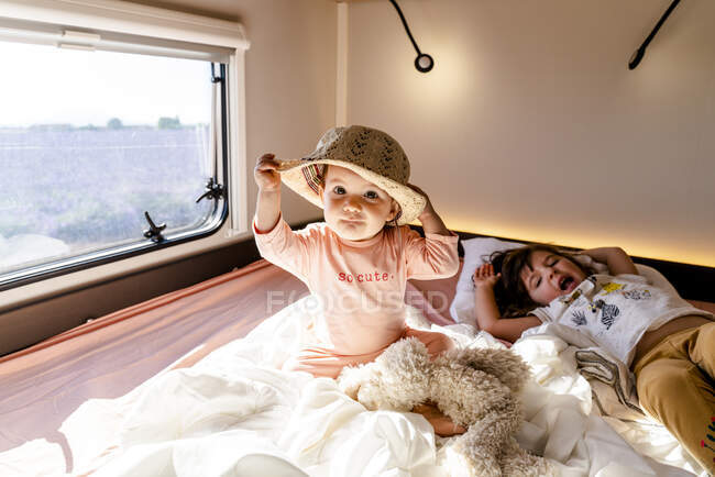 Bonito bebê menina usando chapéu enquanto sentado pela irmã acordar em casa motor — Fotografia de Stock