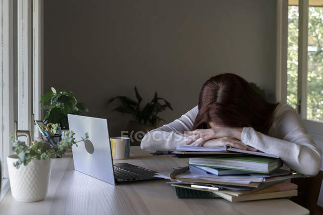 Medico stanco appoggiato su pila di libro mentre seduto a casa — Foto stock