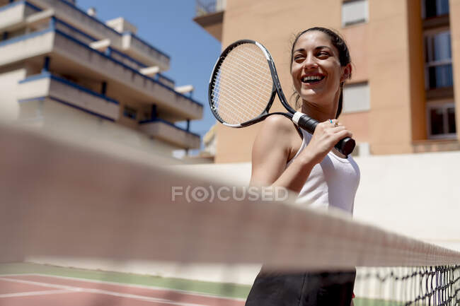 Веселий тенісист тримає ракетку, яка дивиться убік, стоячи навпроти будинків. — стокове фото