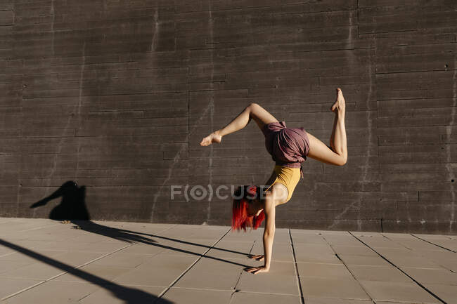 Young woman with red hair performing handstand against black wall — Stock Photo