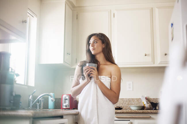 Mulher cuidadosa usando toalha segurando xícara de café enquanto estava na cozinha em casa — Fotografia de Stock
