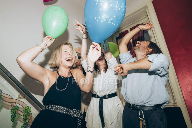 Amigos alegres sosteniendo globos mientras bailan durante la fiesta en casa - foto de stock