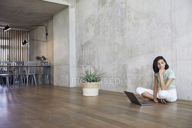 Ragionevole donna d'affari seduta con computer portatile sul pavimento in legno duro contro la parete in ufficio — Foto stock