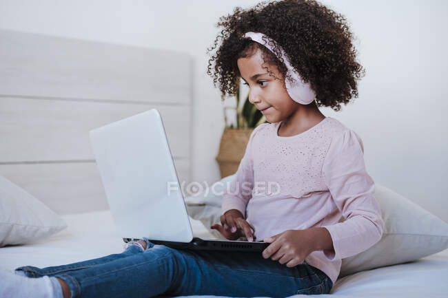 Мила дівчина використовує ноутбук у навушниках для прослуховування музики, сидячи вдома. — стокове фото