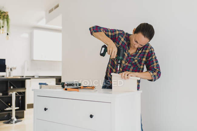 Craftsperson using electric screwdriver while standing by cabinet at home — Stock Photo