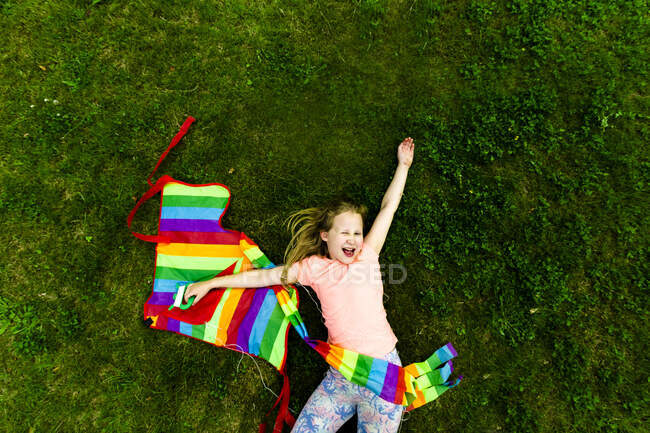 Дівчинка з барвистим змієм радіє, лежачи на траві в парку. — стокове фото