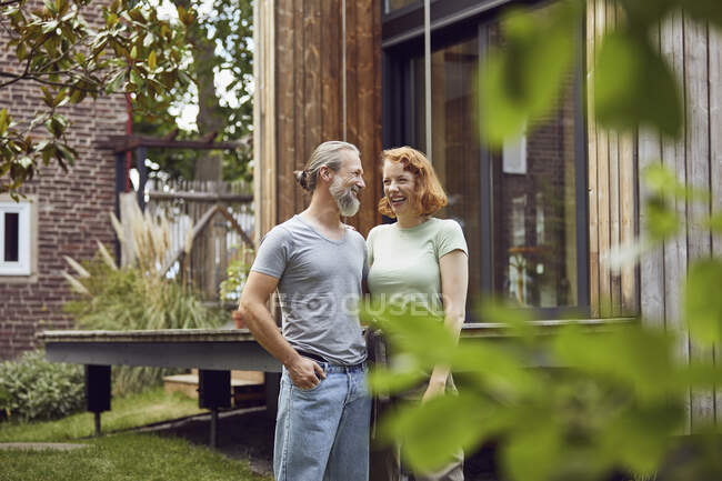 Cheerful couple looking at each other while standing in front of tiny house — Stock Photo