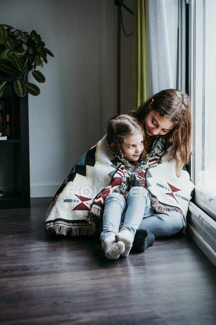 Girl sitting on sitter lap while sitting by window at home — Stock Photo
