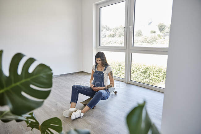 Donna incinta seduta sullo skateboard in una nuova casa — Foto stock