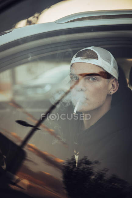 Молодой человек курит сигарету в машине сен через окно — стоковое фото