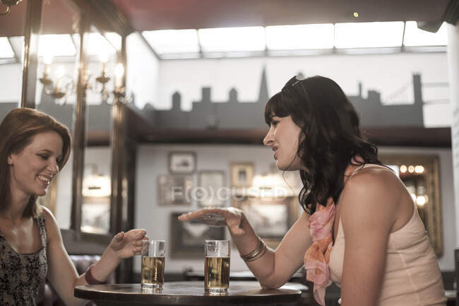 Amigos femininos conversando enquanto bebem cerveja no pub — Fotografia de Stock