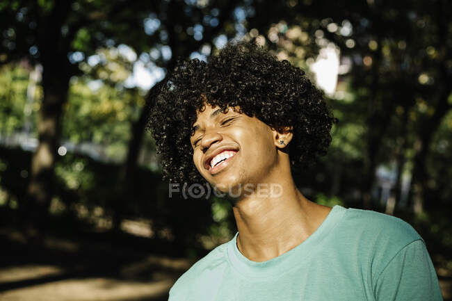 Улыбающийся молодой человек, стоящий в общественном парке в солнечный день — стоковое фото