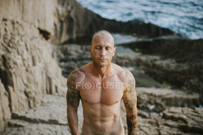 Tattooed Nudist Standing On Volcanic Rocks By The Sea With Closed Eyes Lifestyle Gender