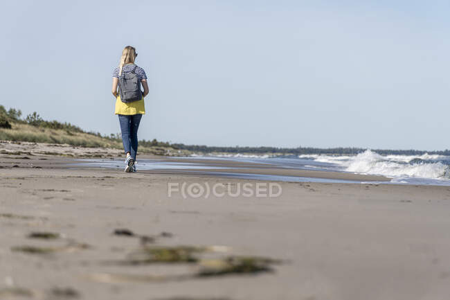 Vue arrière de la femme avec sac à dos marchant sur la plage — Photo de stock