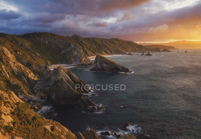 Скалистые скалы в море против драматического неба на закате — стоковое фото