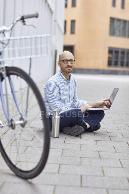 Mitte erwachsener Mann arbeitet auf Laptop, während er auf der Straße sitzt — Stockfoto