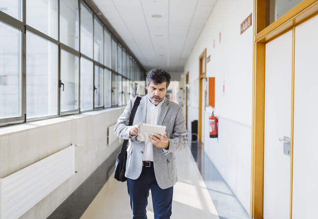 Профессор использует цифровой планшет во время прогулки по коридору в университете — стоковое фото