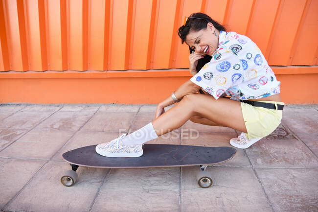 Portrait of beautiful girl crouching beside longboard in front of corrugated iron wall — Stock Photo