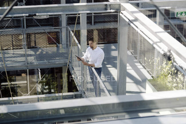 Бізнесмен, використовуючи цифровий планшет, стоїть на перилах пішохідного мосту в теплиці — стокове фото