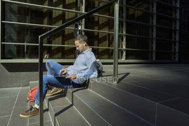 Підприємець з навушниками у вухах, використовуючи ноутбук, сидячи на сходах — стокове фото