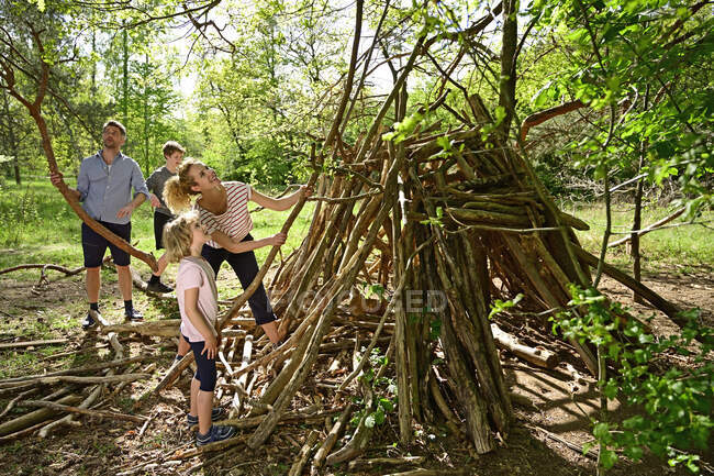 Mother and daughter building camp with father and brother collecting log in background at forest — Stock Photo