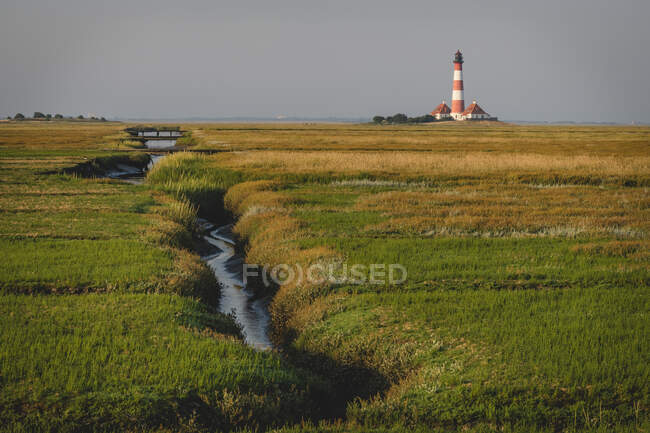 Alemanha, Schleswig-Holstein, Westerhever, Fluxo fluindo através de terreno gramado com Westerheversand farol no fundo — Fotografia de Stock