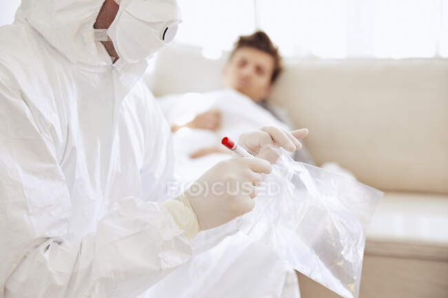 Зблизька лікар тримає медичний зразок у поліетиленовому мішку, а пацієнт лежить на дивані. — стокове фото