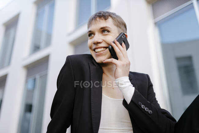 Крупным планом улыбающегося транса, разговаривающего по мобильному телефону, сидя напротив здания — стоковое фото