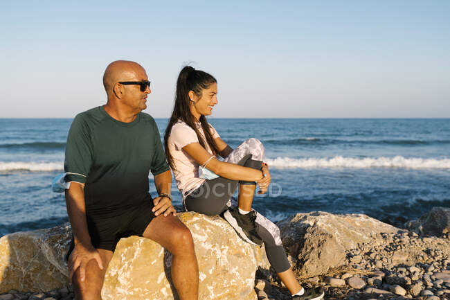 Homem sênior sentado por mulher na rocha contra o mar — Fotografia de Stock