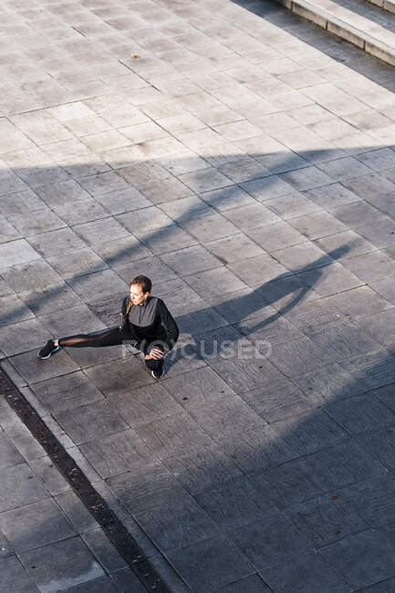 Спортсмен растягивает ноги, приседая на крыше — стоковое фото