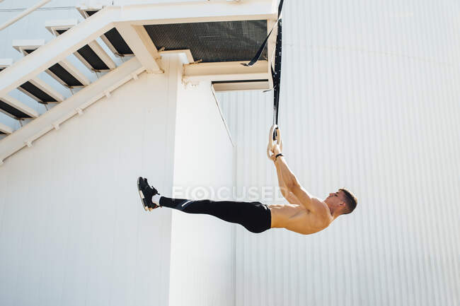 Atleta equilibrando el peso corporal mientras cuelga en el anillo en la escalera al aire libre - foto de stock