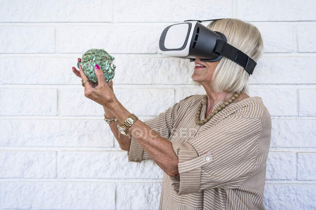 Senior woman holding conch, using virtual reality simulator — Stock Photo
