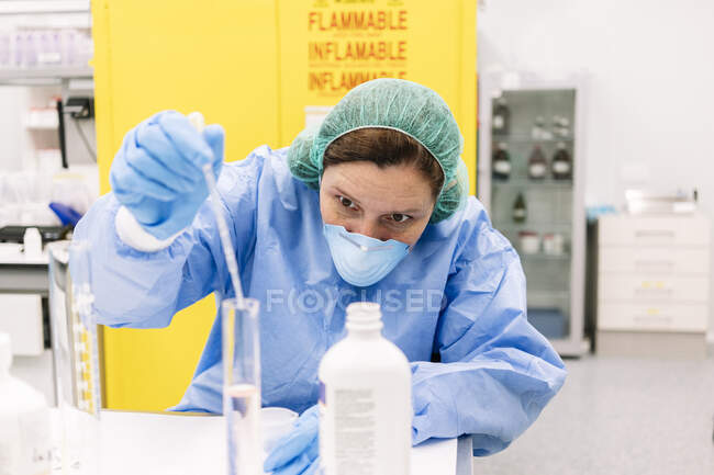 Farmacéutica femenina mezclando productos químicos en cilindro graduado en laboratorio - foto de stock