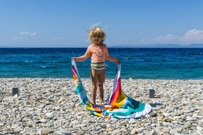 Porträt eines kleinen Mädchens, das mit Handtuch in der Hand am felsigen Strand steht — Stockfoto