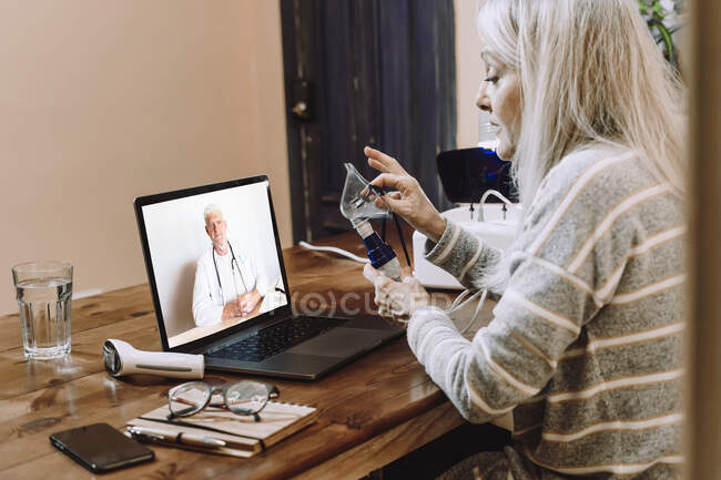 Старшая женщина на видео-вызове с врачом говорит о распылителе дома во время COVID-19 — стоковое фото