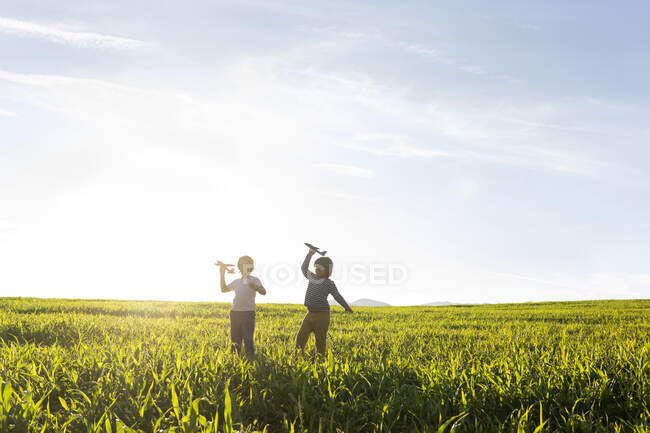 Boys playing with airplane toy while standing on grass in meadow — Photo de stock