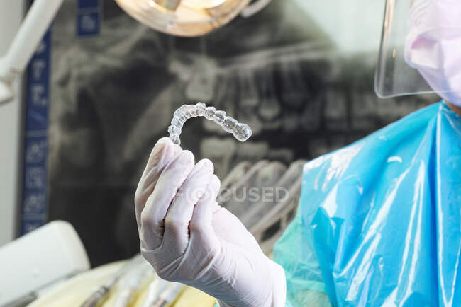 Dentiste portant une combinaison de protection tenant l'aligneur dentaire en main à la clinique — Photo de stock