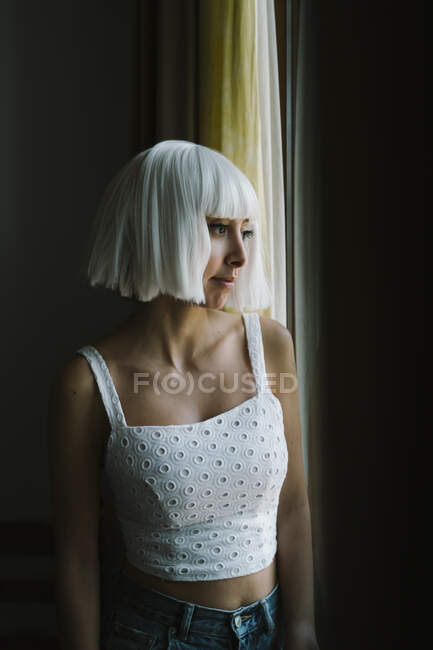 Junge Frau schaut durch Fenster, während sie zu Hause steht — Stockfoto