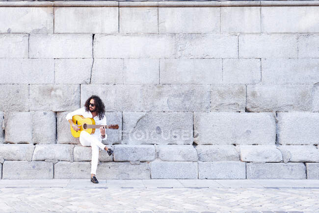 Guitarist playing guitar while sitting against concrete wall — Stock Photo