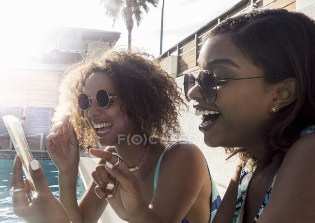 Allegro giovani amici femminili condividere ricordi su smart phone a bordo piscina — Foto stock