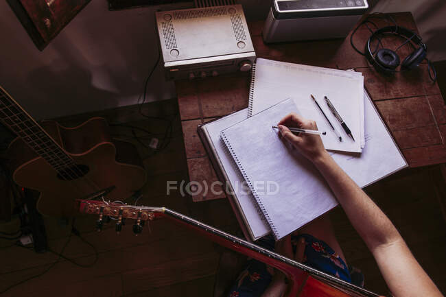 Giovane donna che scrive nel libro mentre pratica la chitarra a casa — Foto stock