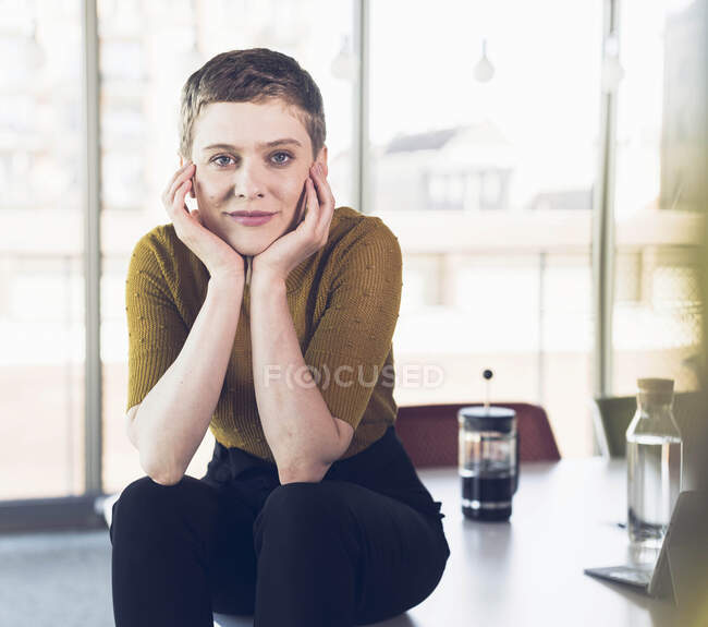 Портрет усміхненої ділової жінки, яка сидить на столі в офісі. — стокове фото